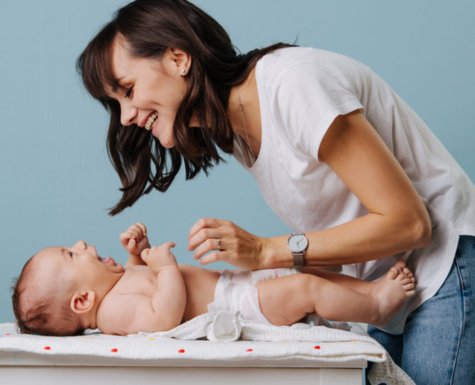 Mama preoblači otroka na previjalni podlogi Mama preoblači otroka na previjalni podlogi